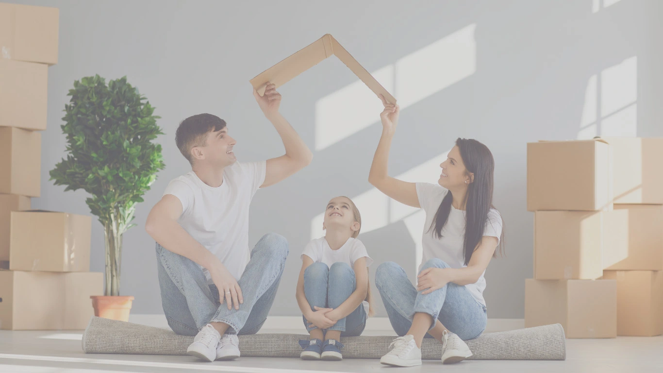 Young family sitting on floor with moving boxes, making a cardboard roof – concept of life insurance as a safety net.