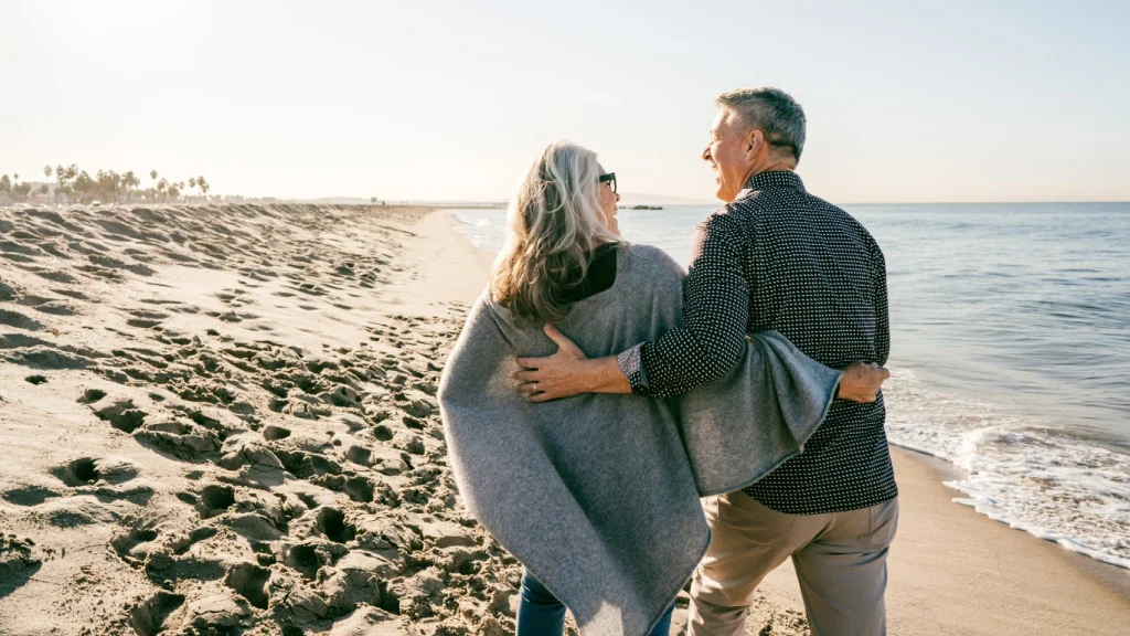 Senior couple embracing while walking on the beach – symbolizing lifelong partnership and term life coverage.