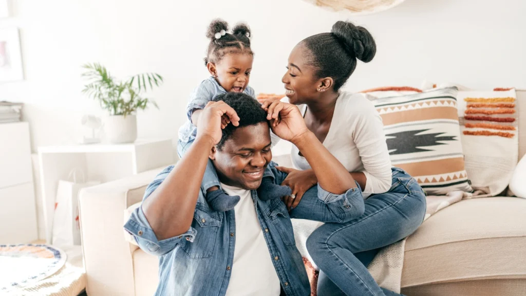 Black family playing together on a couch at home – emotional protection through life insurance coverage.