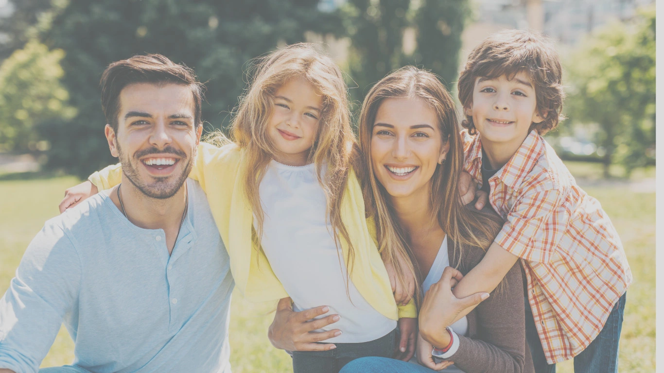Happy young family smiling outdoors in a park on a sunny day – symbol of life insurance protection.