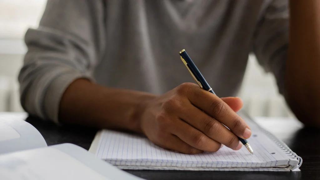 Person writing in a notebook — applying for term life insurance or taking notes on policy options.